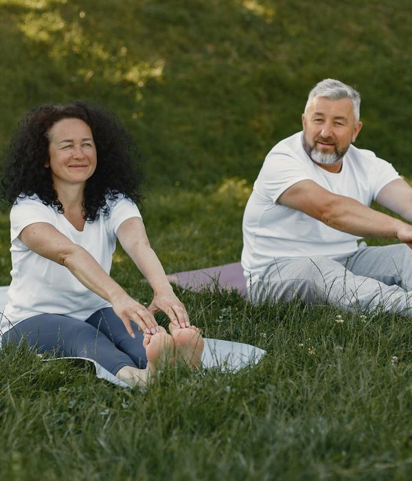 Smiling woman stretching gently outdoors in a green park setting.